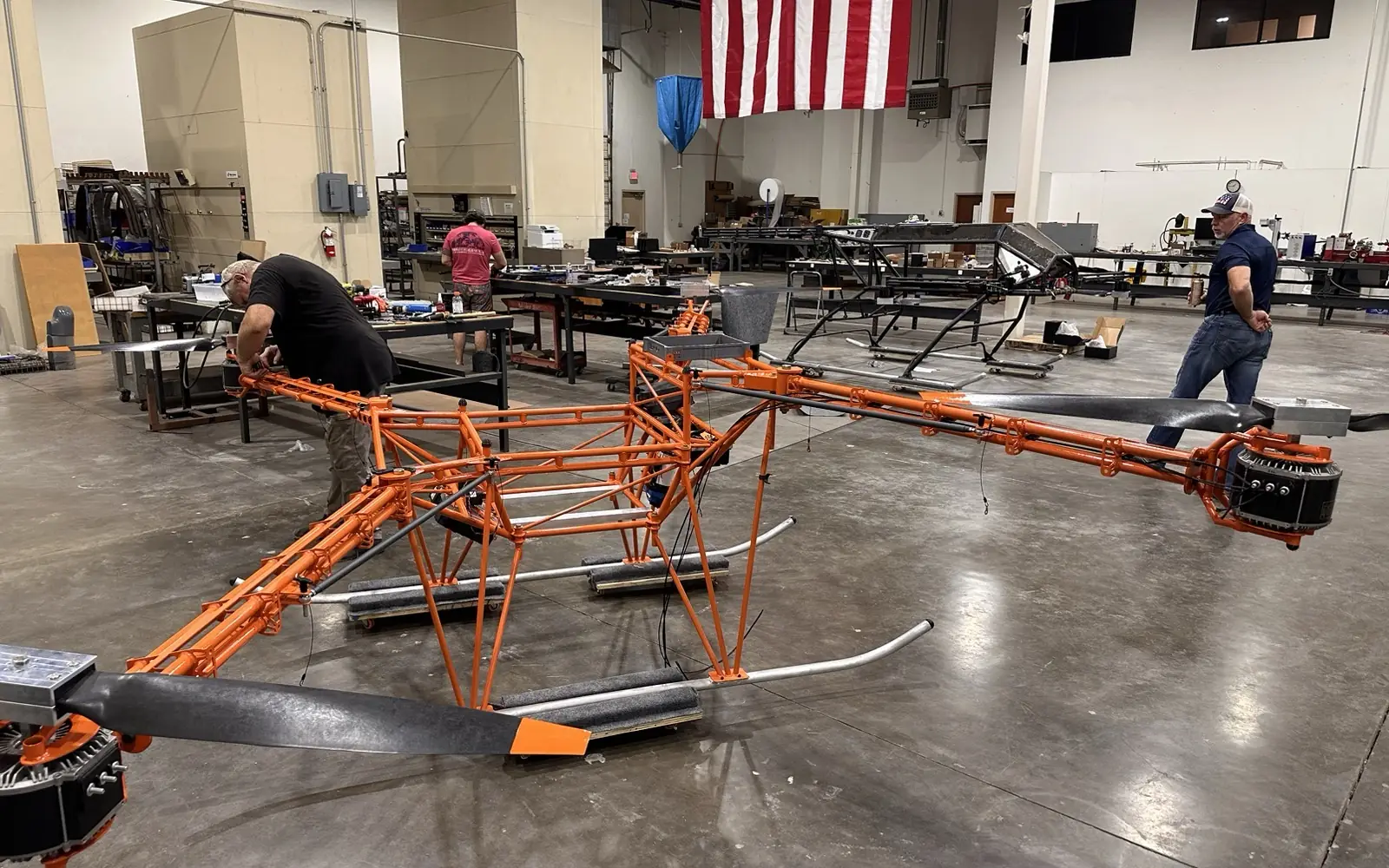 Harvest 100 airframes in assembly on the shop floor, one painted orange, under a large American flag