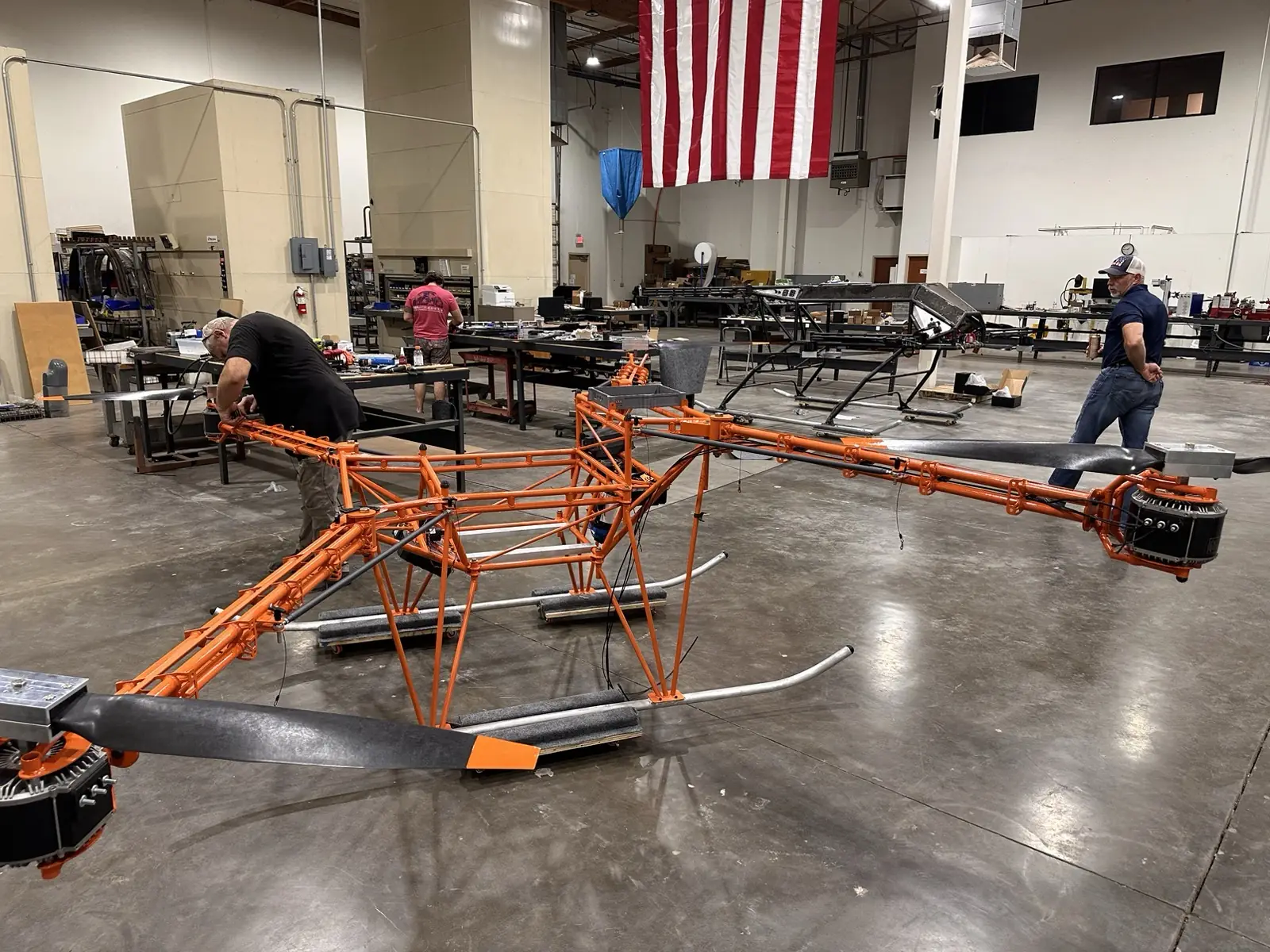 Harvest 100 airframes in assembly on the shop floor, one painted orange, under a large American flag